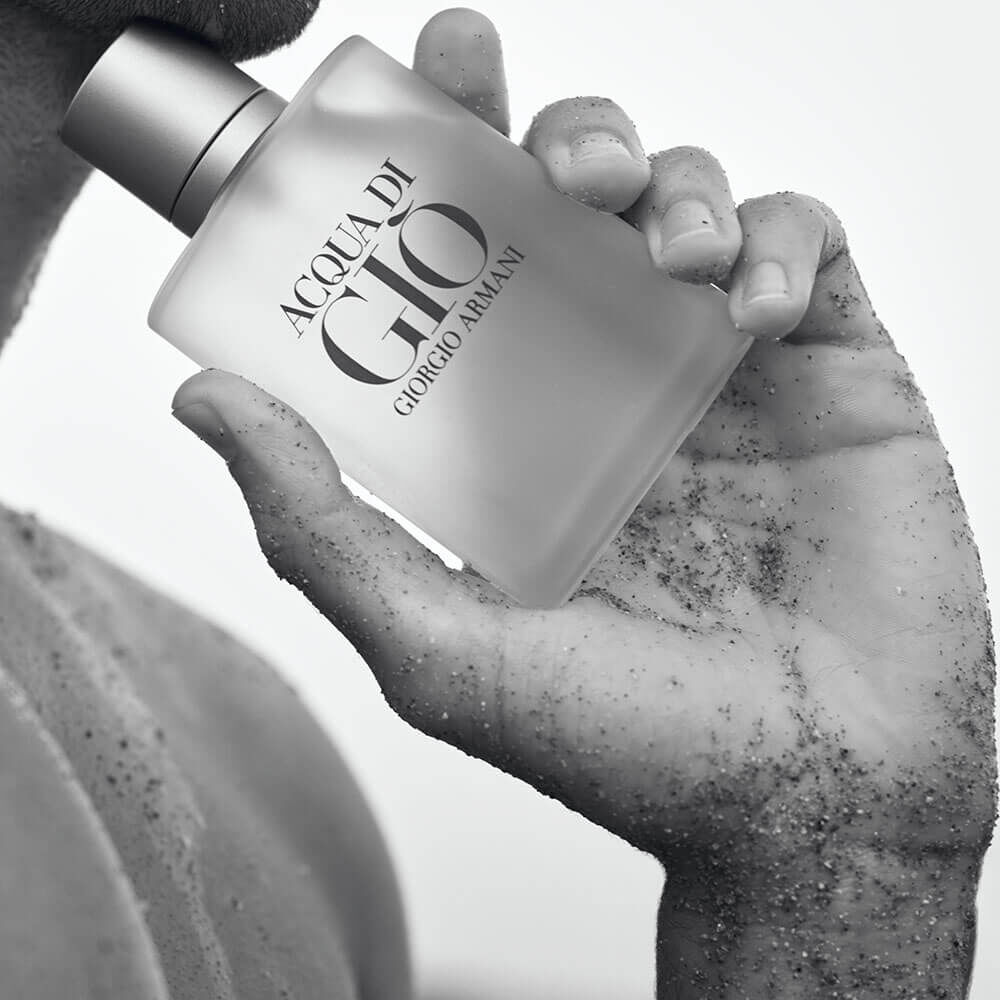 Acqua di Giò na mão: pele bronzeada com grãos de areia segurando o frasco fosco — preto e branco