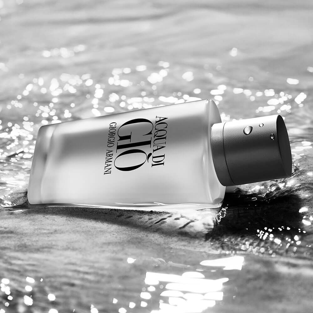 Detalhe: frasco Acqua di Giò repousado em água rasa, com reflexos prateados B&W