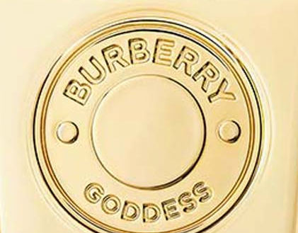 Close-up do medalhão dourado em relevo BURBERRY GODDESS sobre o vidro transparente