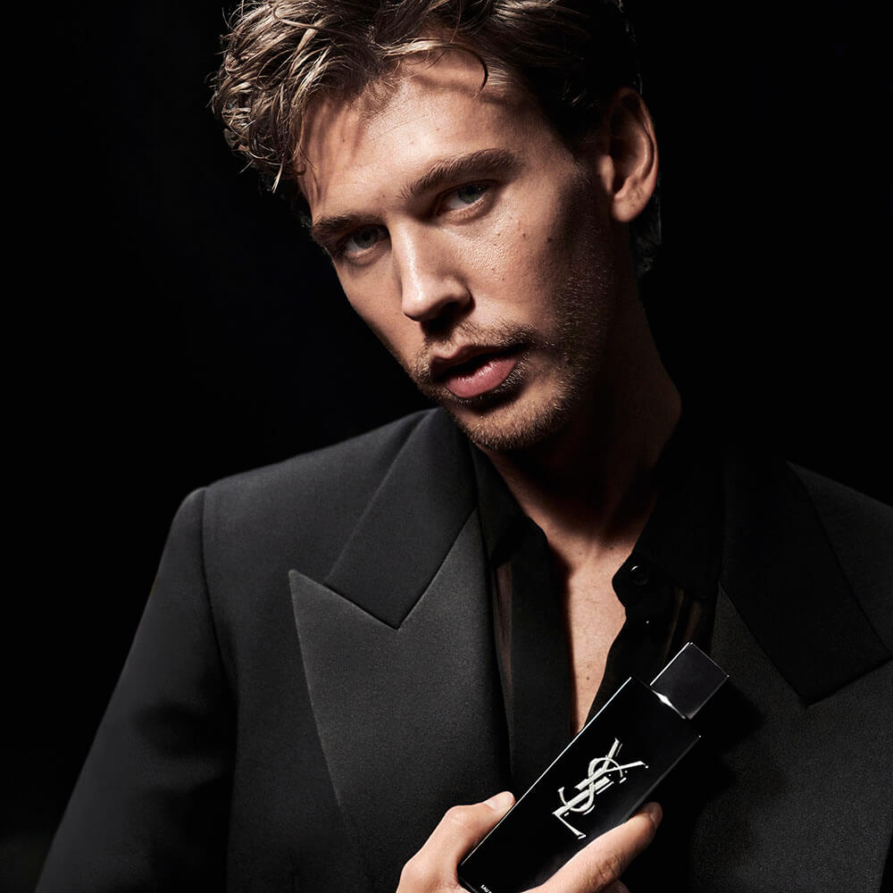 Austin Butler, embaixador da campanha YSL MYSFL, em alfaiataria preta, segurando o frasco MYSFL Eau de Parfum.