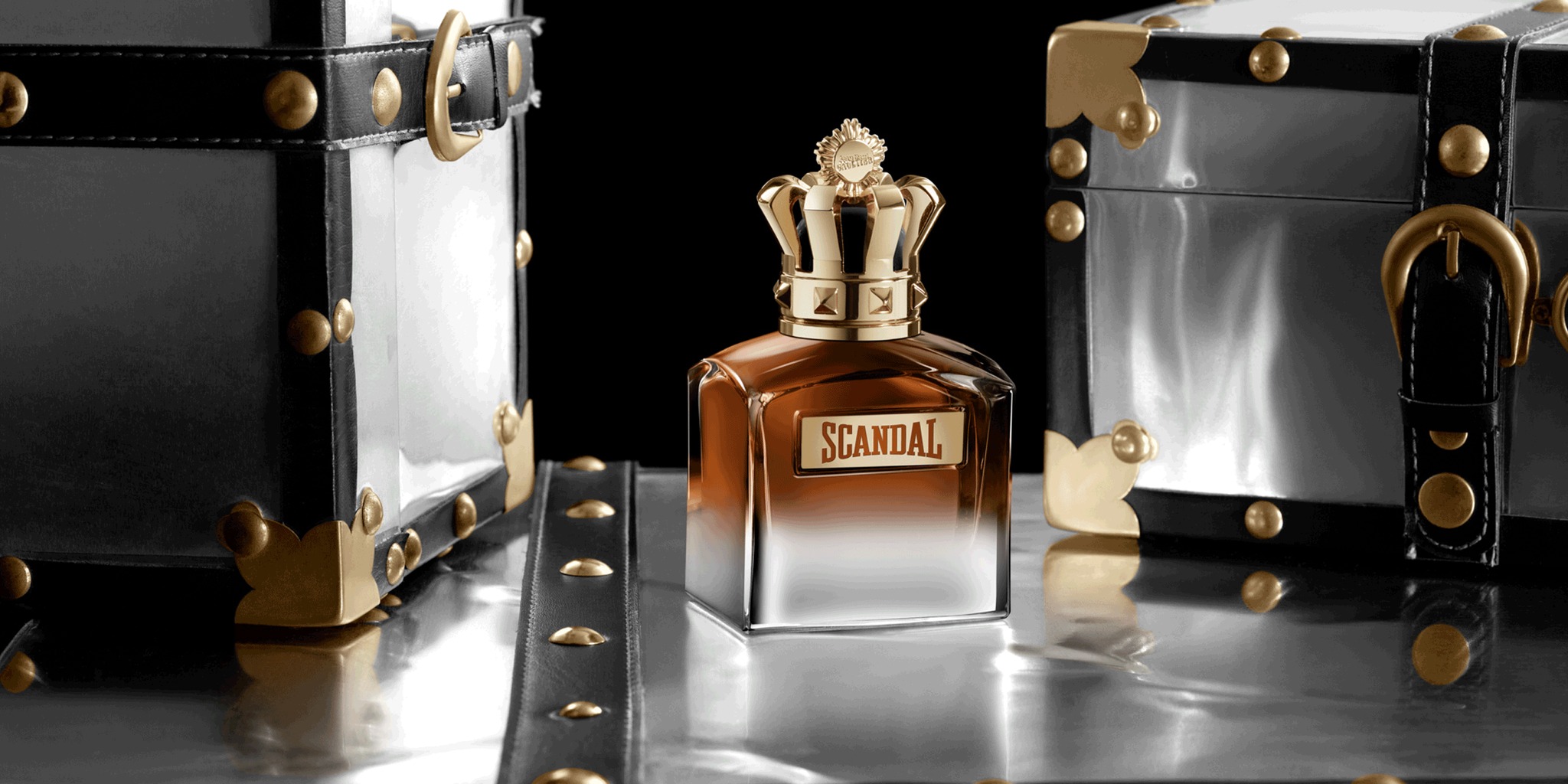 Scandal pour Homme Elixir 50ml entre duas malas pretas com ferragens douradas — cena oficial Jean Paul Gaultier do Scandal Express.