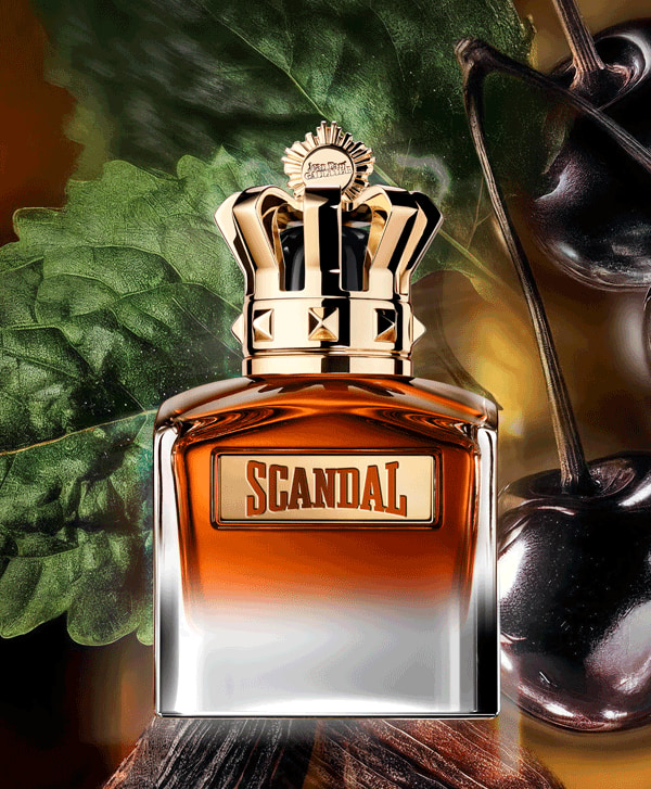 Composição oficial Scandal Elixir mostrando o frasco coroado entre cerejas pretas, folhas escuras e madeira — três matérias-primas saturadas da fórmula JPG.