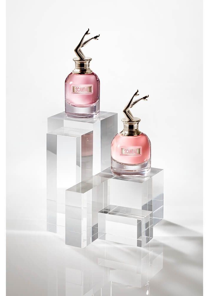 Cena Scandal: frasco em torso feminino rosa com coroa dourada, ao lado de favo de mel, laranja sanguínea cortada e gardênia branca