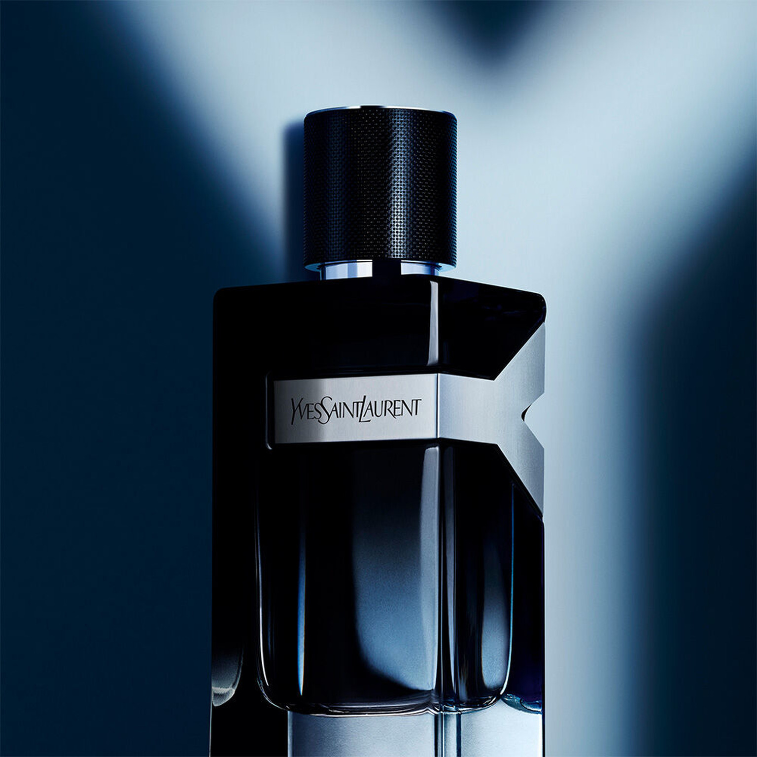 Y Eau de Parfum em close: frasco com gradiente azul-marinho recortado por feixes de luz cruzados em forma de Y sobre fundo azul-noite